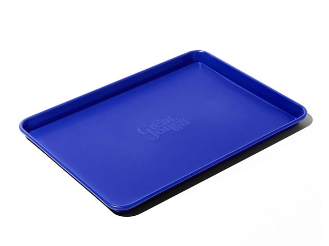 A bright cobalt blue Great Jones Holy Sheet half sheet pan with the brand name stamped in its center