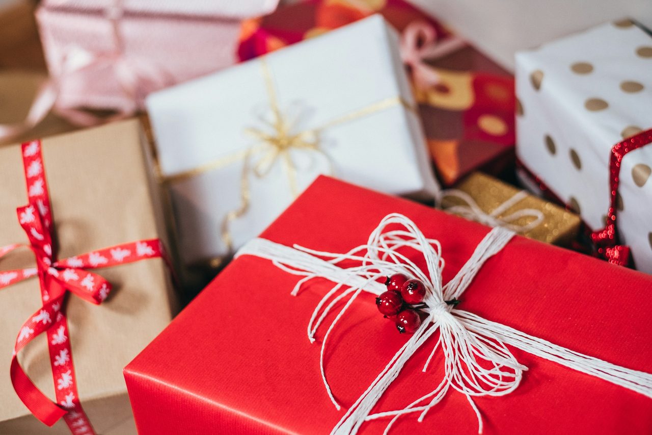 A pile of wrapped presents: a red box tied with white string and berries, kraft paper with a red ribbon, gold polka dots