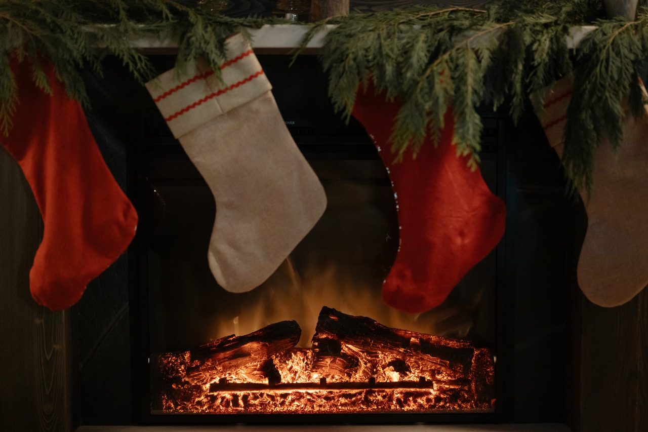 Red and linen Christmas stockings hanging under a pine garland in front of a glowing fireplace