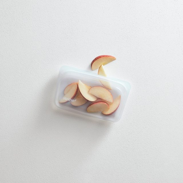 A clear Stasher silicone snack bag holding sliced apples