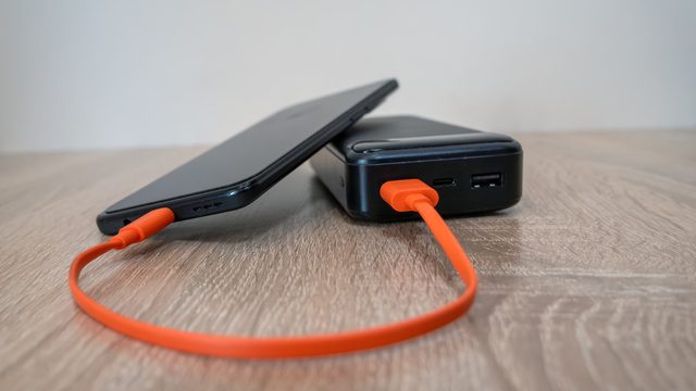 A smartphone resting on a black power bank, charging through an orange USB-C cable, with a USB-A port beside it