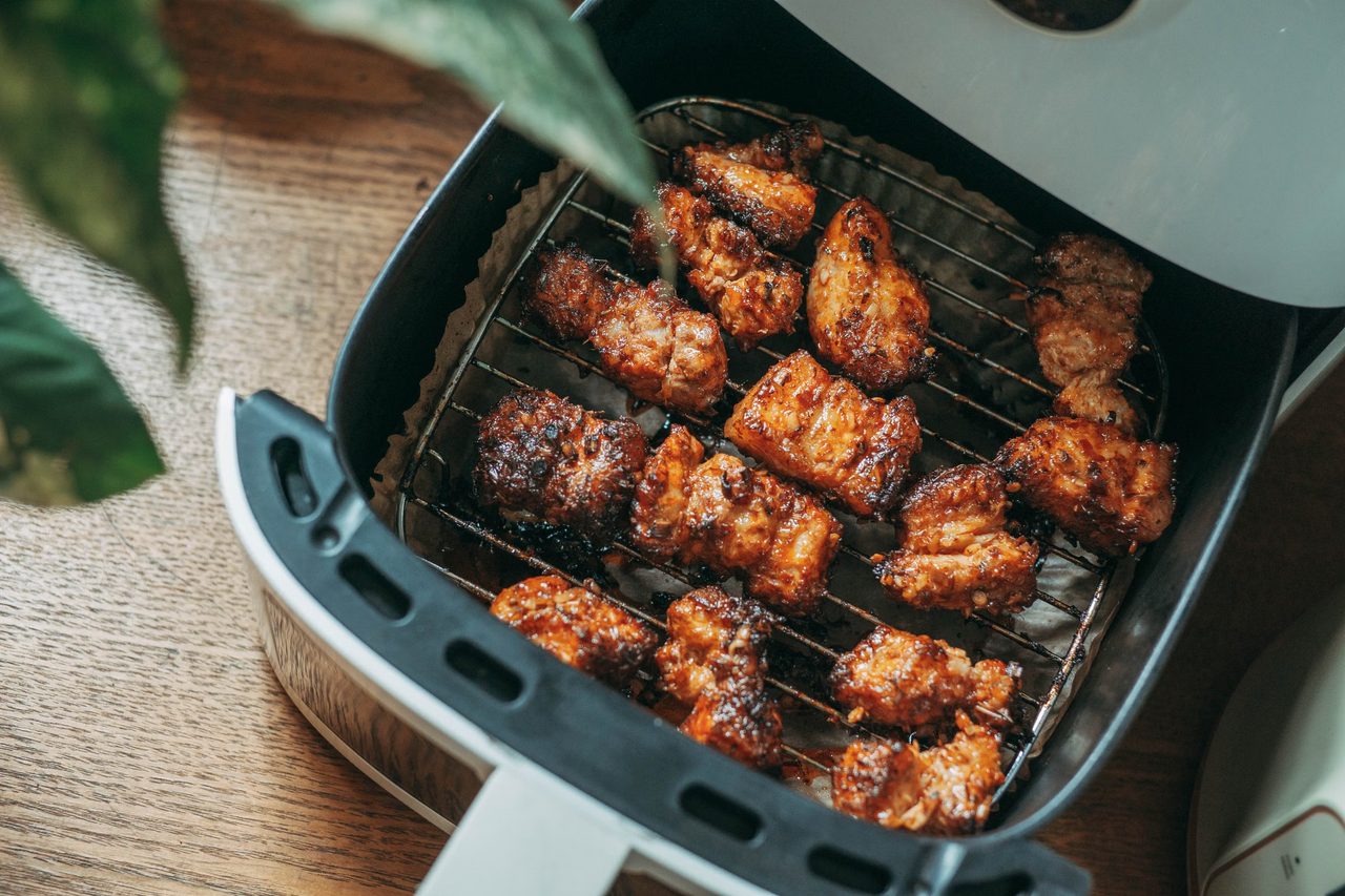 Browned chicken pieces on a rack in the open basket of a white air fryer, on a wooden counter
