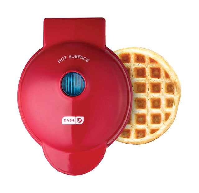 A small round red Dash Mini Waffle Maker with a golden waffle beside it