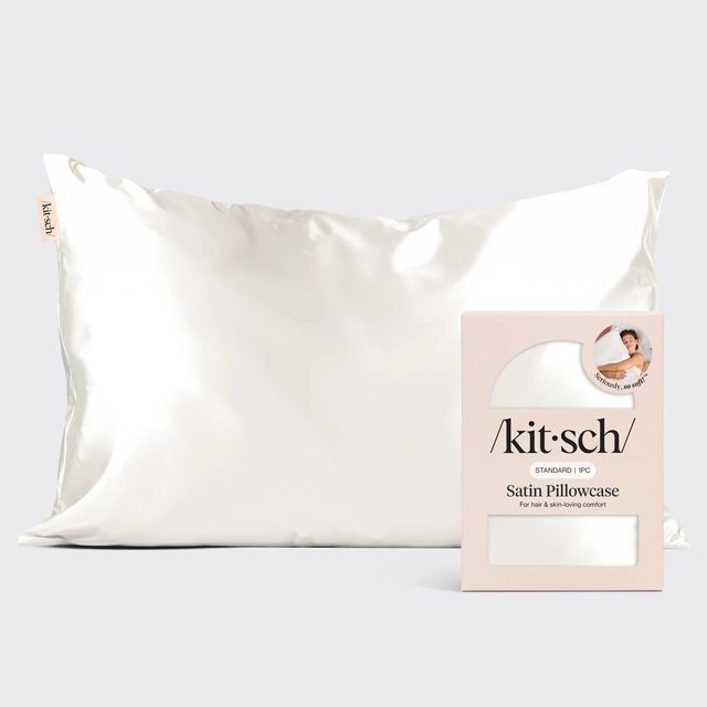 An ivory Kitsch satin pillowcase on a pillow, next to its small pink and white box